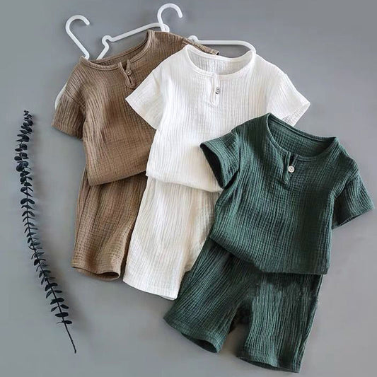 Boy and girl baby short-sleeved summer suits in brown, white, and green, displayed on hangers against a grey background.